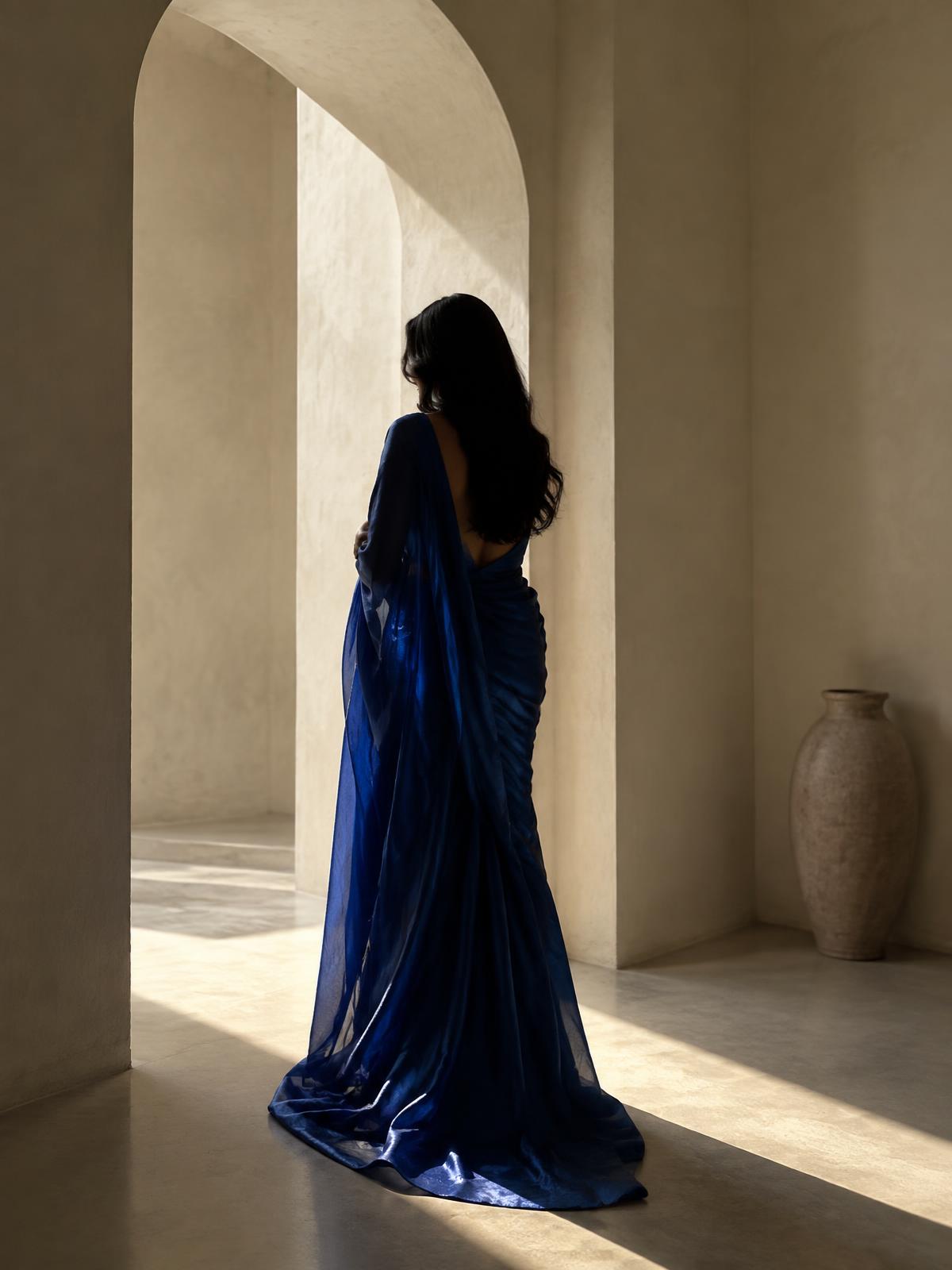 Silhouette of a woman in a flowing royal blue saree within an ivory arched interior